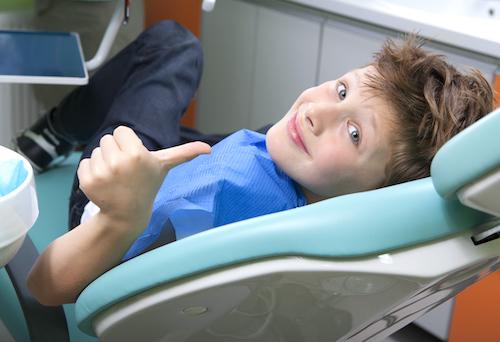 A child in the dentist's chair giving the thumbs up